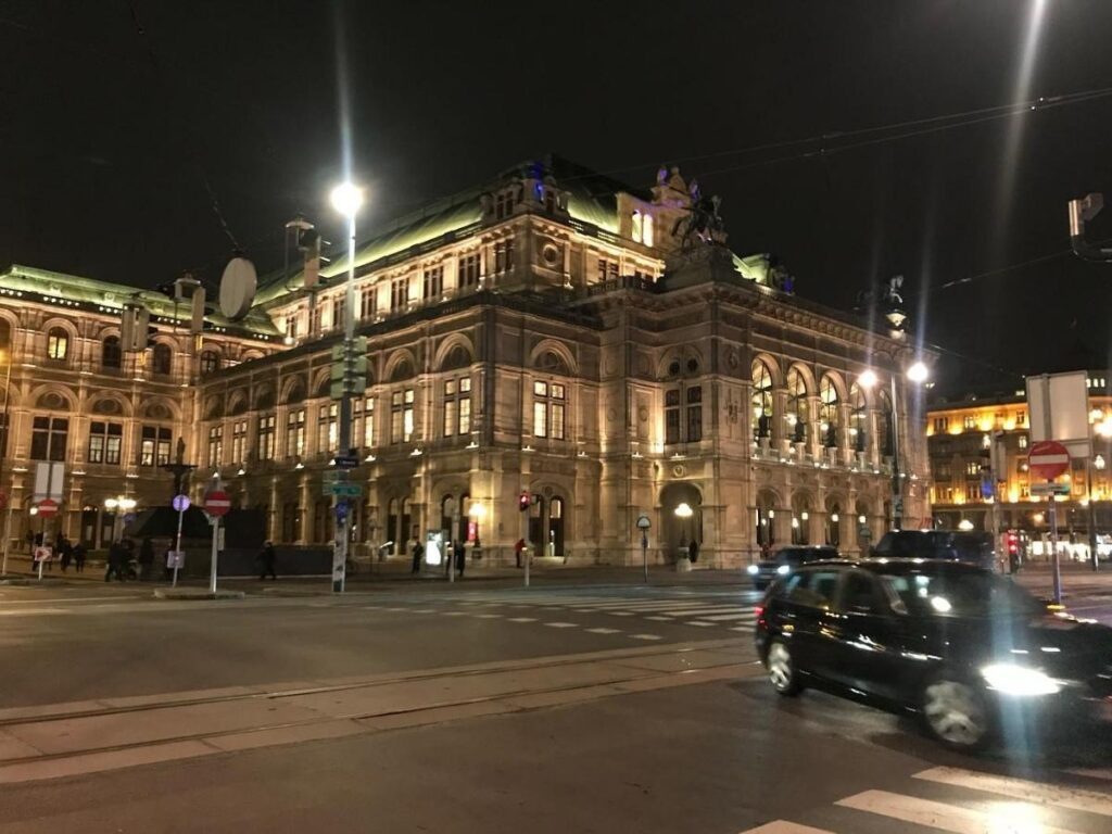 The Vienna State Opera illuminated at night with people arriving for a performance