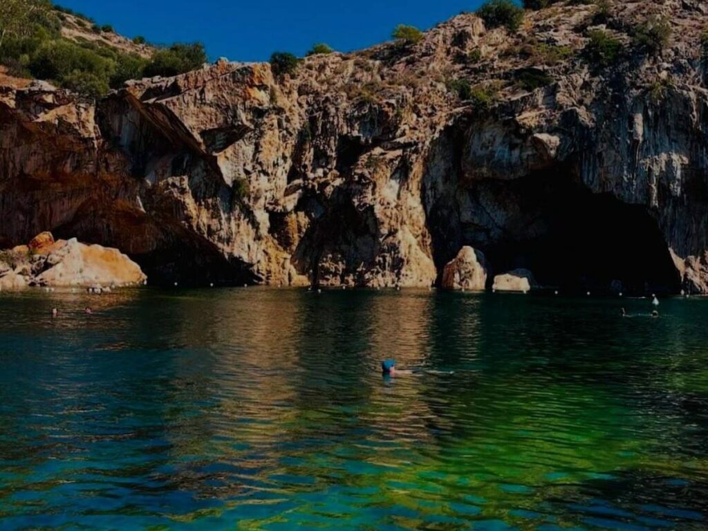 Swimmers in a small Vouliagmeni cove with turquoise water and rocky edges