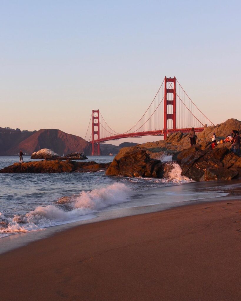 Golden Gate Bridge during sunset from Baker Beach with warm light reflecting on the sand