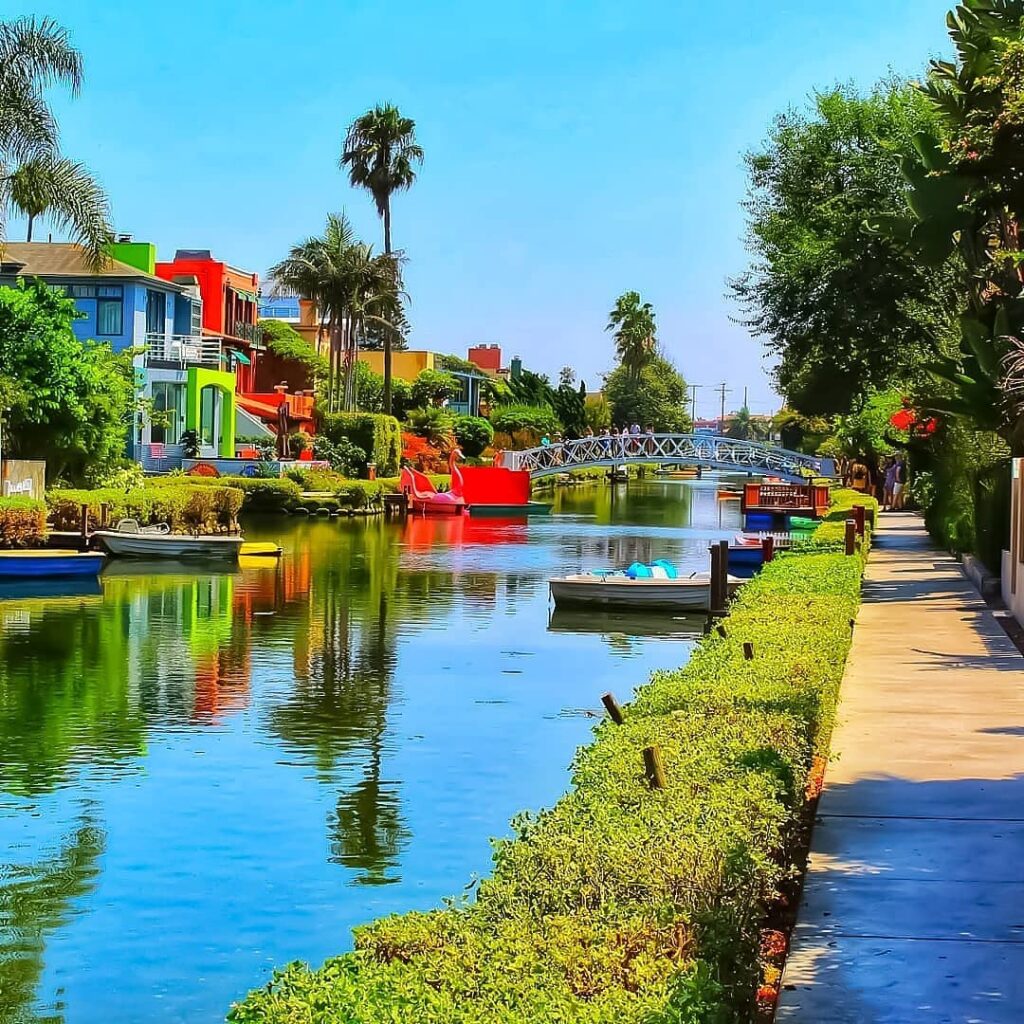 Arched pedestrian bridge over peaceful Venice Canals surrounded by homes and greenery