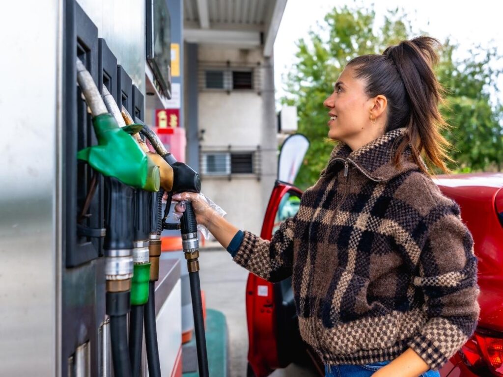 Gas pump display showing fuel prices with car being filled up during road trip