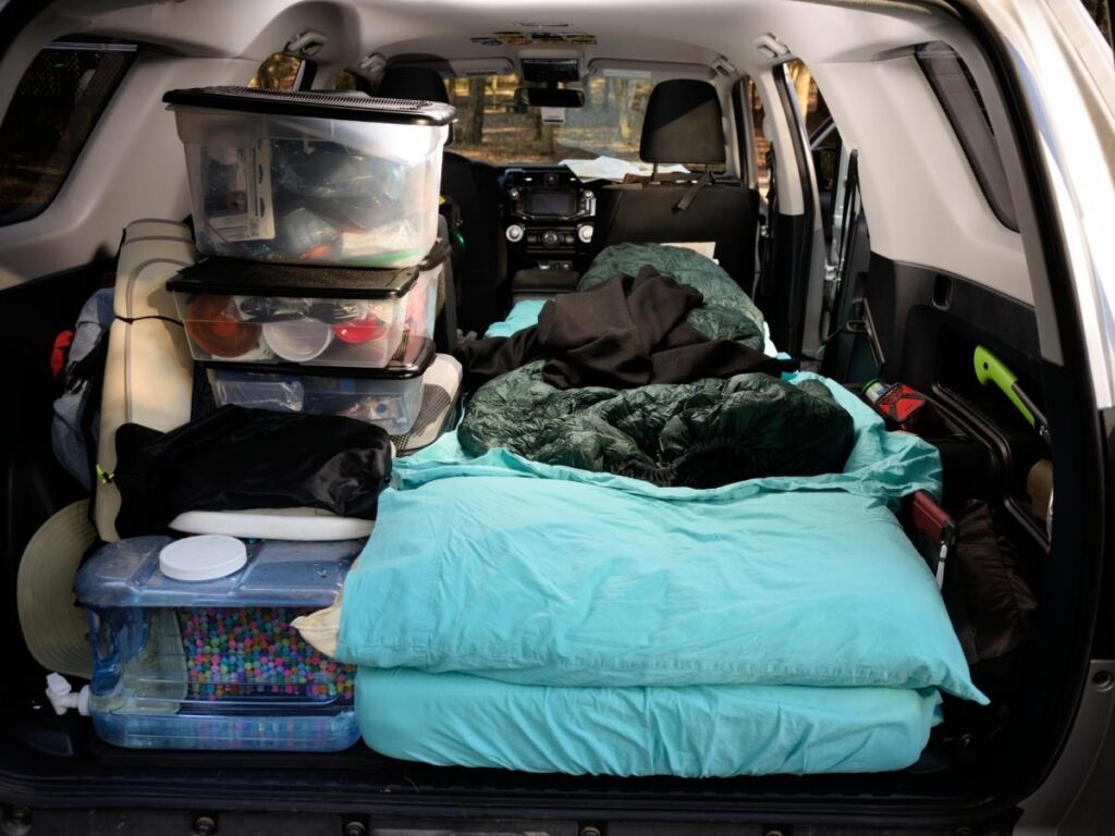 SUV car camping setup with sleeping pad and blankets in the back of the vehicle