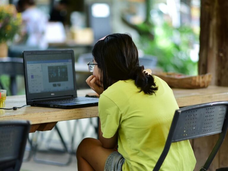 Person working on a laptop at an outdoor café in a sunny destination during a workcation
