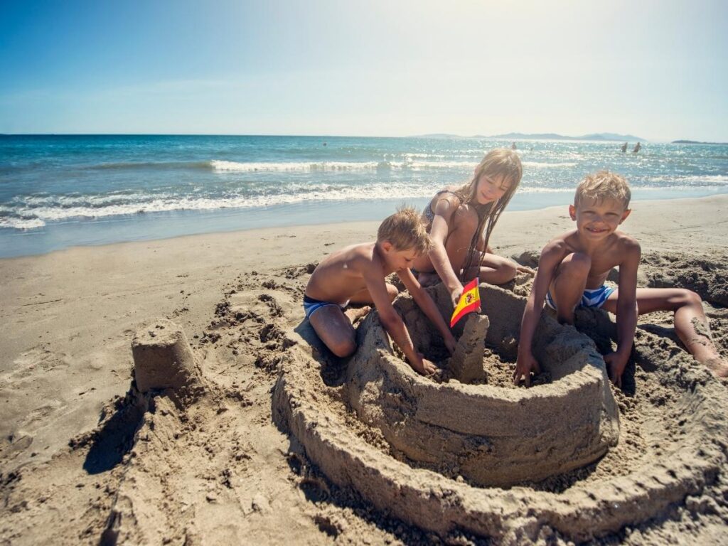 Family with children building small modest sandcastle on European beach