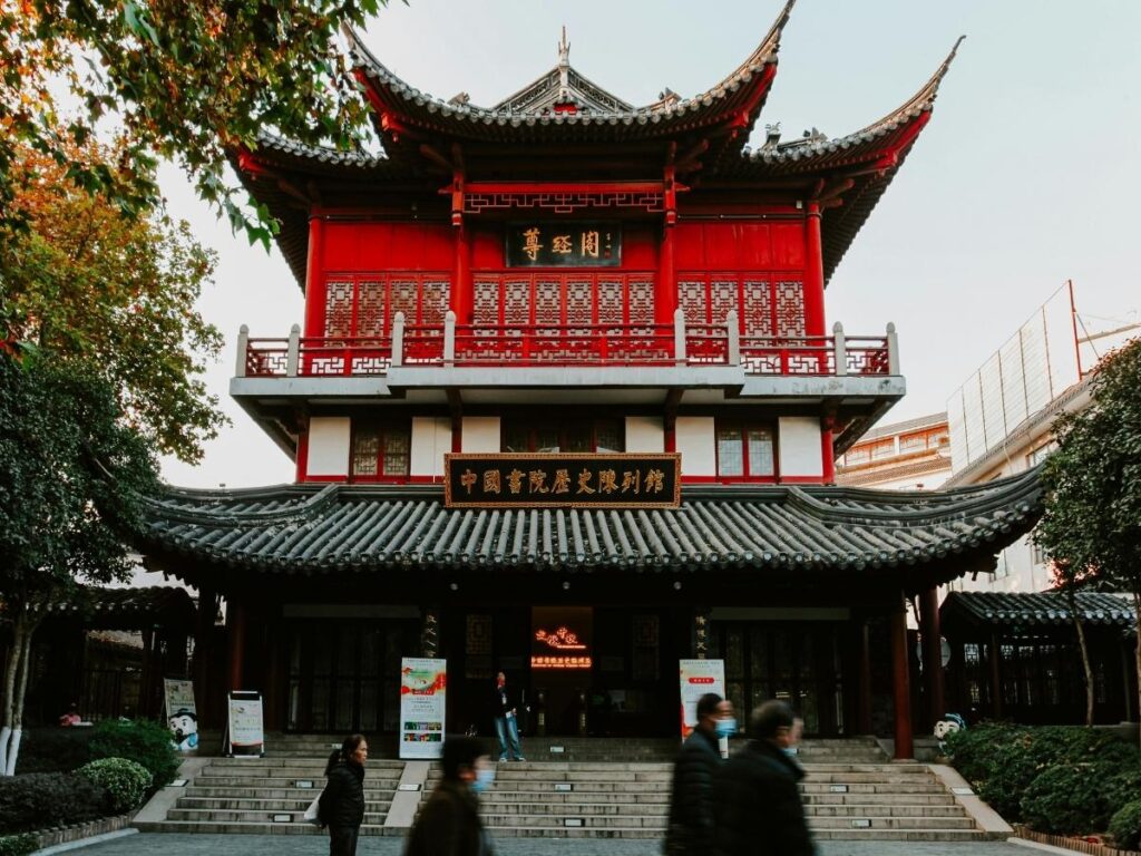 Person on a smartphone in front of a traditional Chinese gate or street with blocked app icons representing China's Great Firewall internet restrictions