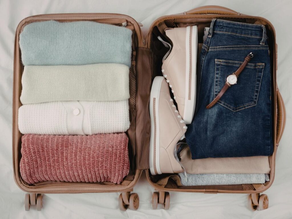 Open suitcase packed with folded heavy winter clothes including sweaters, jeans, and a coat