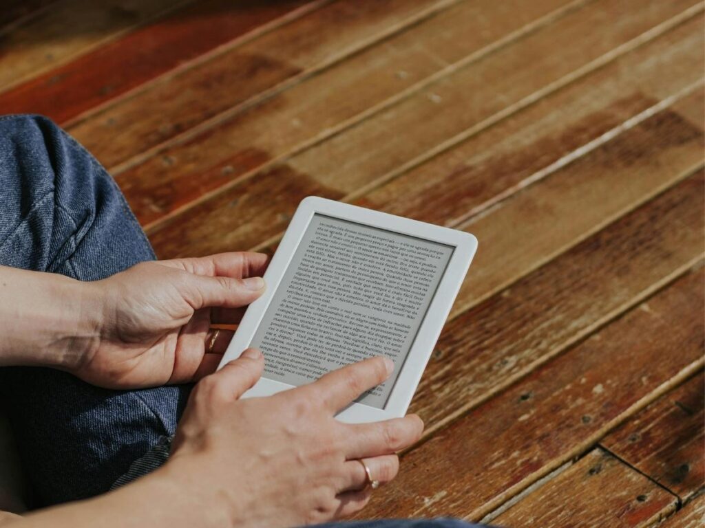 Kindle Paperwhite e-reader on beach towel with sunglasses