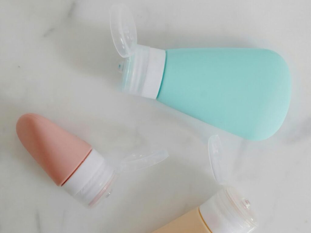 Set of silicone leak-proof toiletry bottles laid out next to a clear TSA toiletry bag