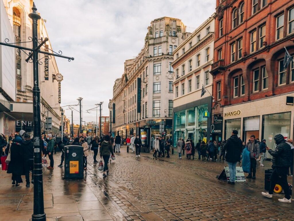 Rainy street in Manchester, England with pedestrians and local shops on a grey afternoon