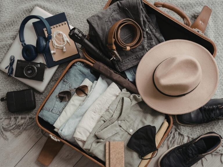 Open suitcase with clothes and travel items laid out on a bed before packing