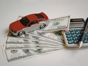 Person planning road trip budget with map and calculator next to packed car on scenic highway