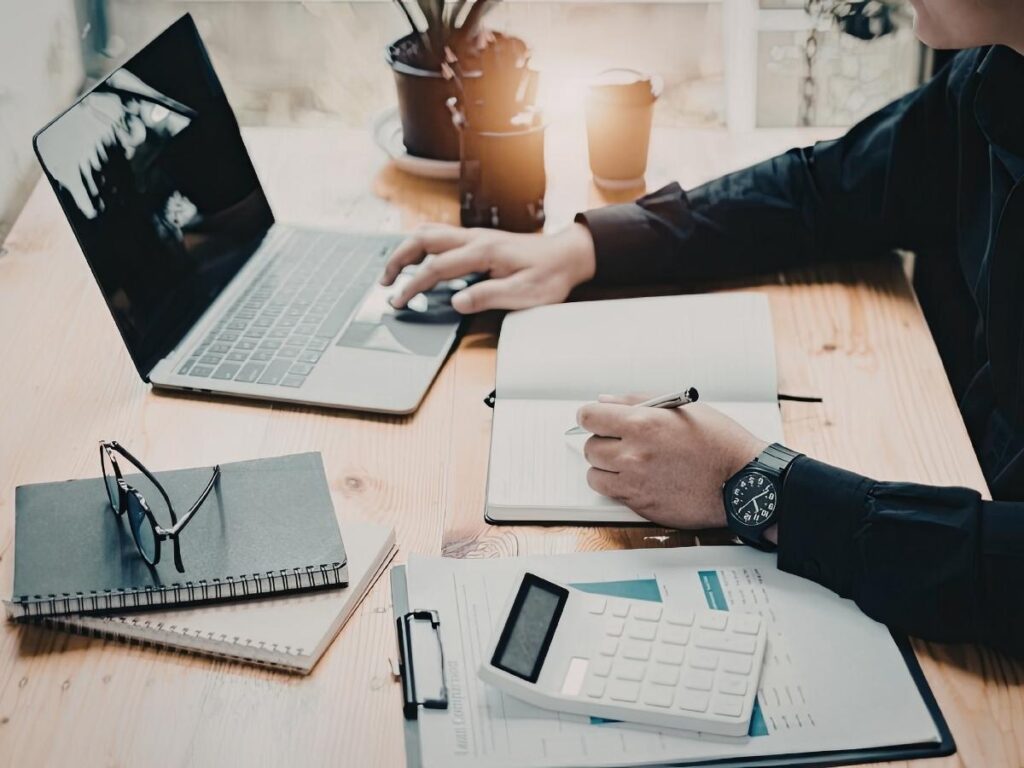 Travel blogger researching on a laptop at a desk surrounded by travel books and a notebook representing online content creation