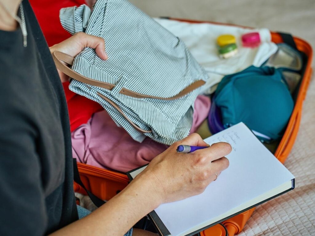 Traveler writing a packing checklist in a notebook next to an open suitcase