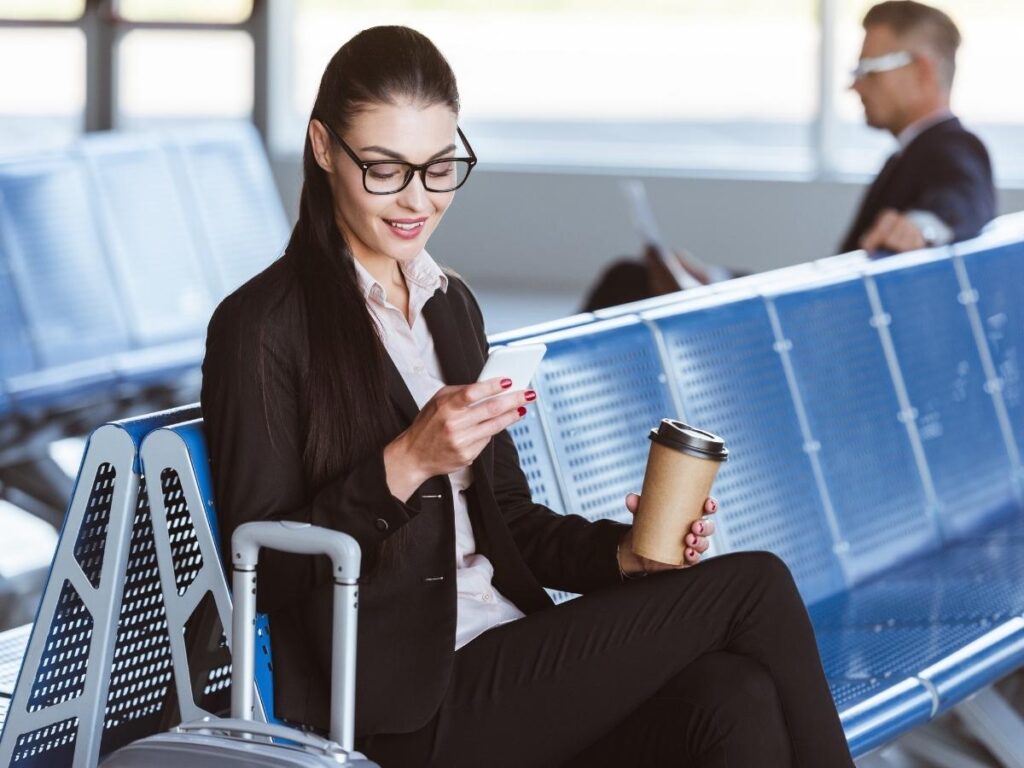 Traveler using a smartphone in a busy airport lounge connected to public Wi-Fi with other passengers in the background