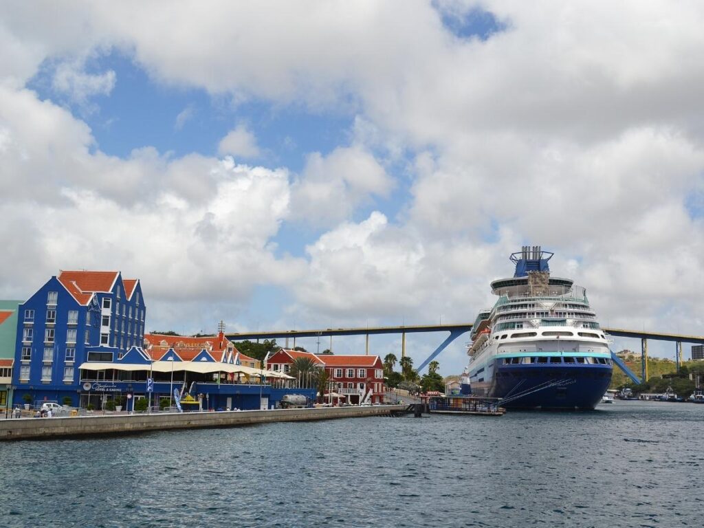 A cruise ship docked near a turquoise Caribbean island with clear blue water
