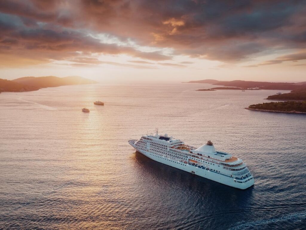 Cruise ship sailing past a coastal European town at sunset