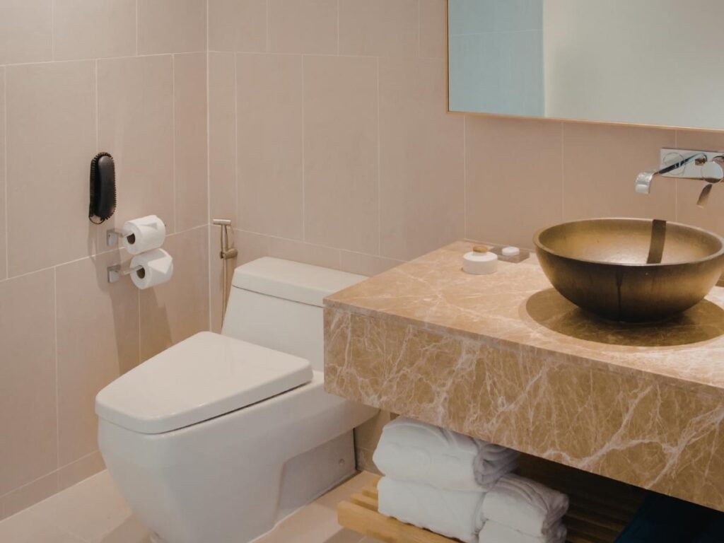 Clean hotel bathroom with toilet toilet paper holder and vanity counter close together