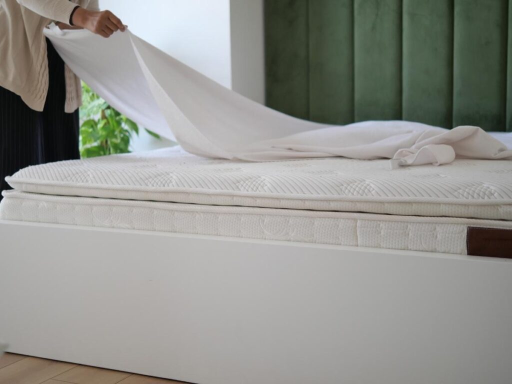 Traveler pulling back hotel bed sheets to inspect mattress and clean white linen