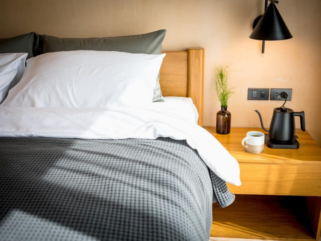 Hotel room coffee maker and electric kettle on a wooden tray beside the bed