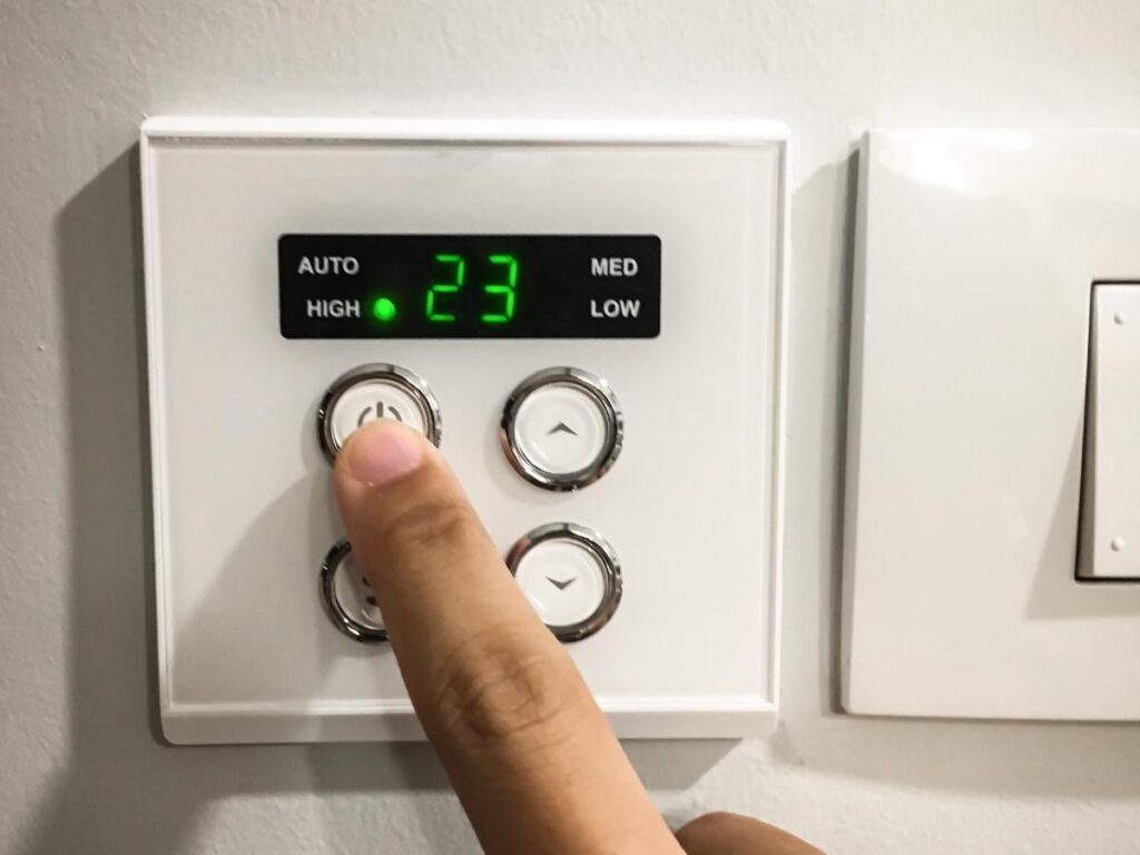 Hand adjusting a hotel room thermostat to a cooler temperature for better sleep