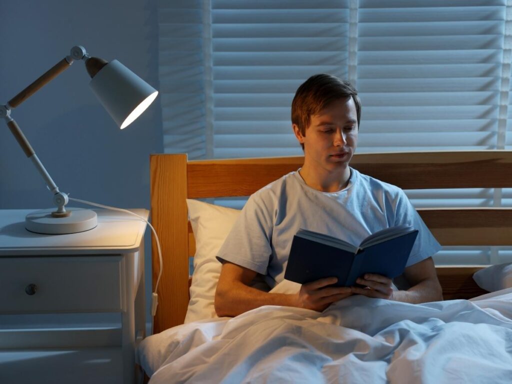 Person sitting calmly on a hotel bed reading a book before sleep with a warm bedside lamp