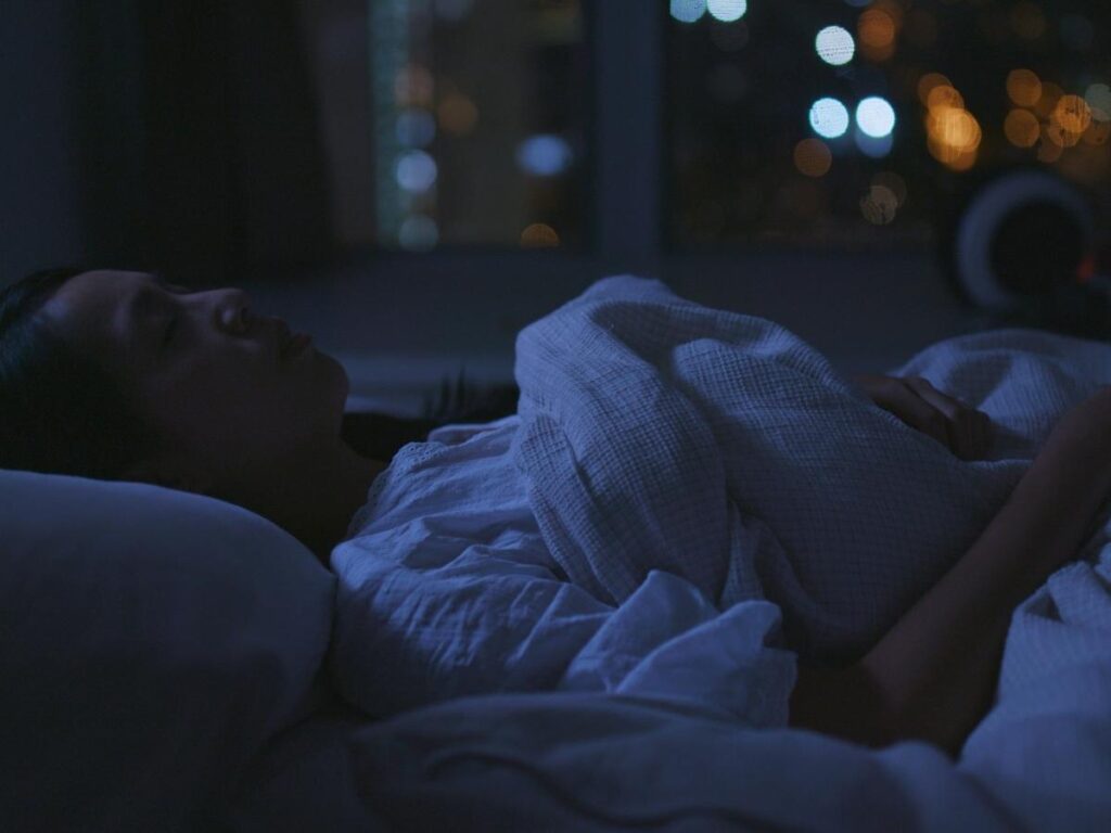 Traveler lying awake in a dark hotel room staring at the ceiling at night