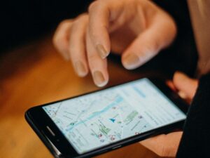 Person holding a smartphone with Google Maps open showing a city neighborhood map while planning a trip