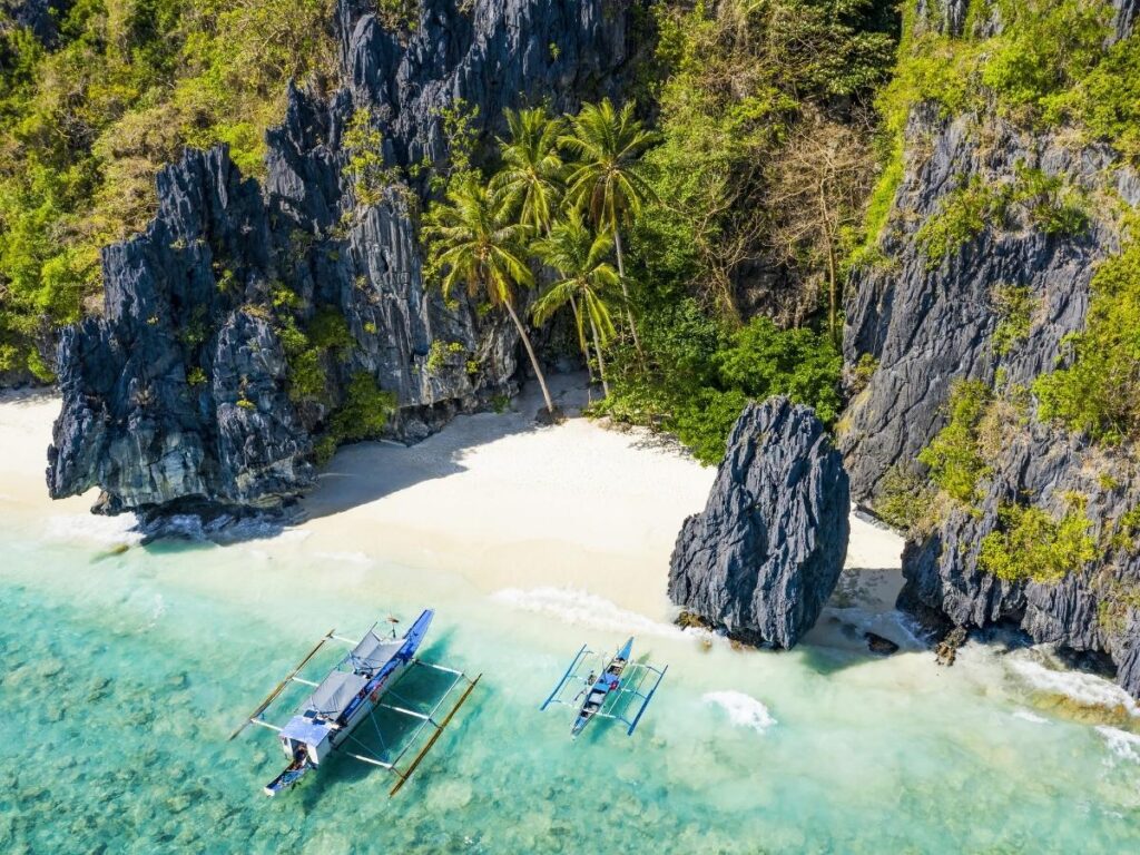 Pristine white sand beach with clear blue water surrounded by jungle in Palawan Philippines