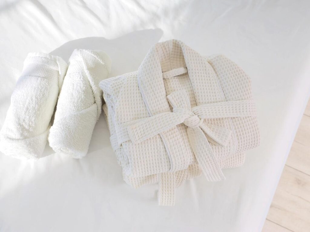 Luxury hotel room with neatly folded white towels bathrobe and amenities on the bed