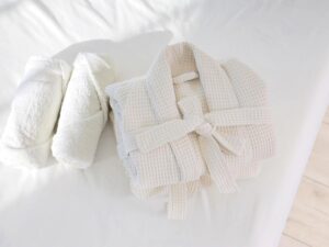 Luxury hotel room with neatly folded white towels bathrobe and amenities on the bed