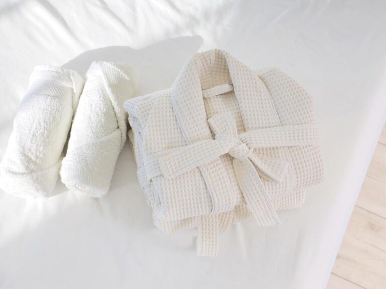 Luxury hotel room with neatly folded white towels bathrobe and amenities on the bed