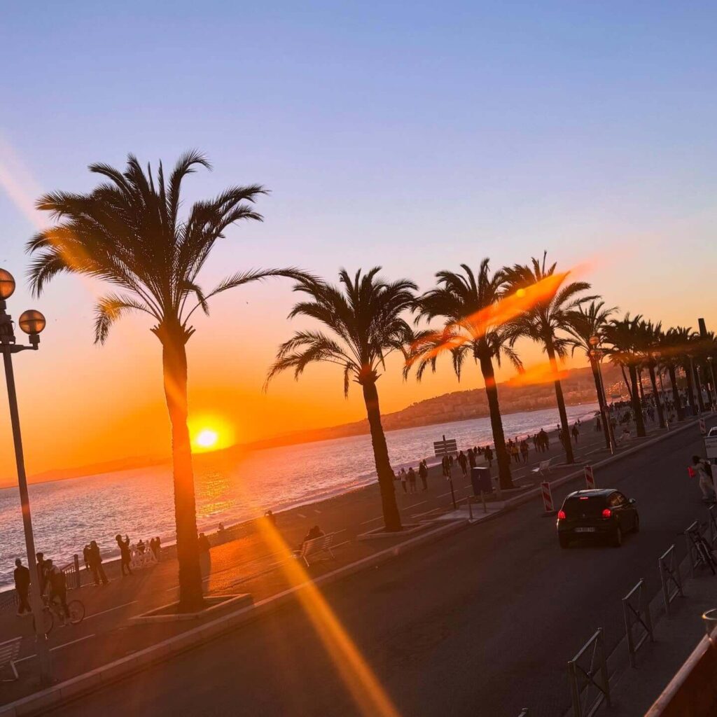 Golden hour light along the promenade in Nice with people walking by the sea