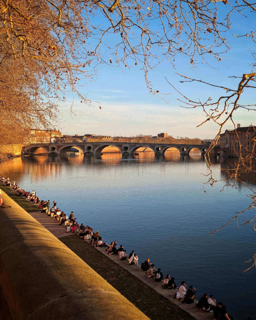 People gathering by the river in Toulouse during a summer evening