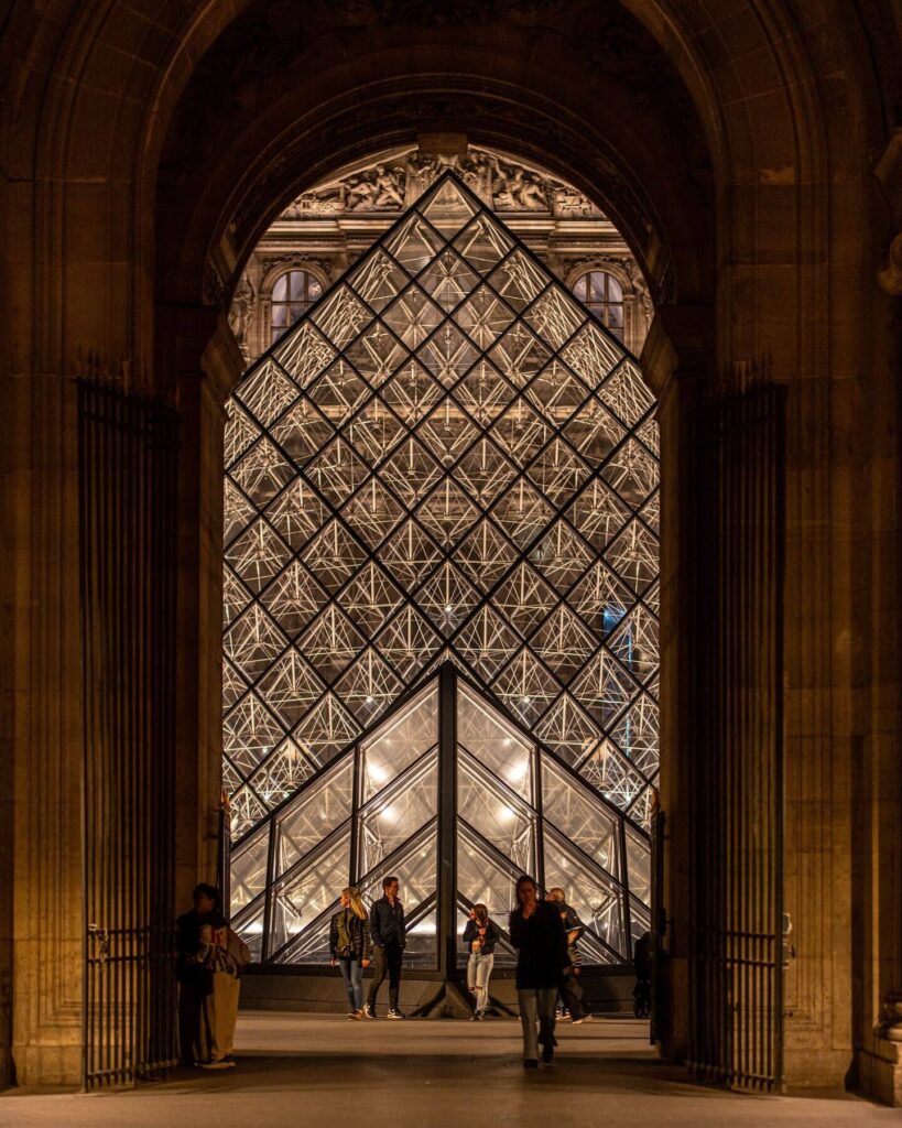 Visitors walking through a long gallery inside the Louvre Museum