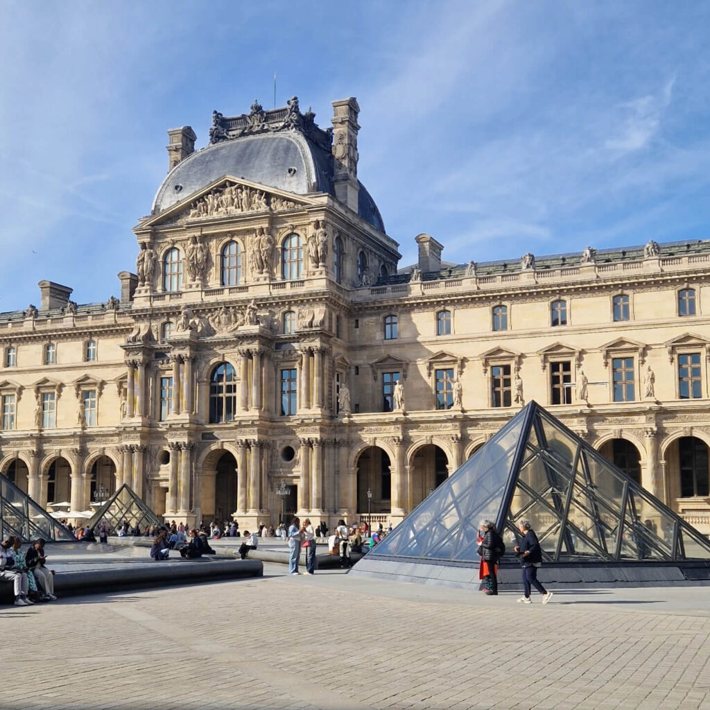 Crowds and long lines outside the Louvre pyramid entrance during midday