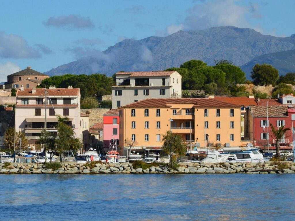 Saint Florent marina with boats, waterfront restaurants, and hills in background