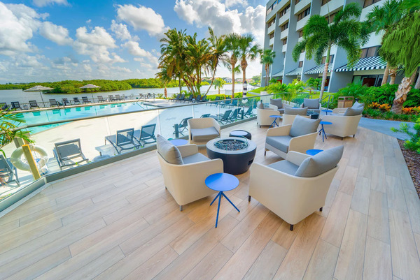 Waterfront view of DoubleTree by Hilton Tampa Rocky Point featuring modern coastal-style architecture, bayfront scenery, palm trees, outdoor pool area, and relaxing sunset ambiance near Tampa Bay.