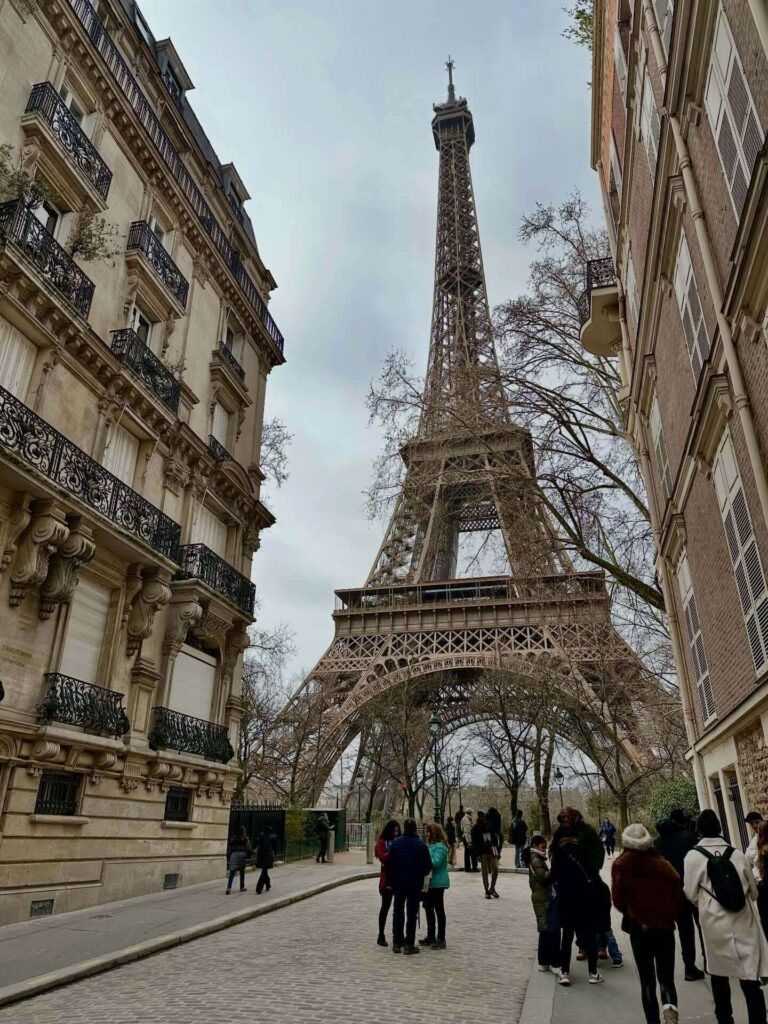 Eiffel Tower appearing between Paris buildings from a street perspective