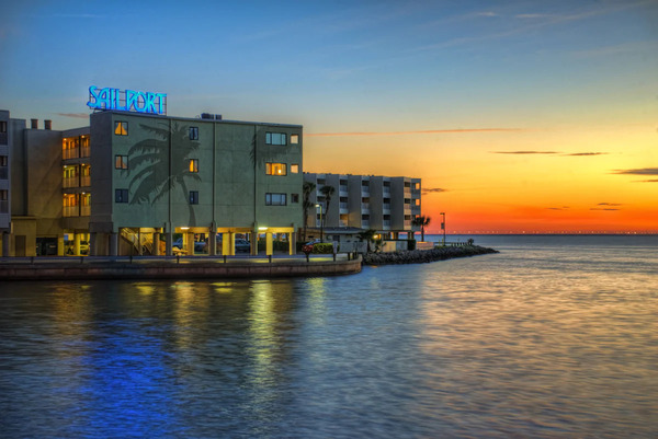 Waterfront balcony view at Sailport Waterfront Suites featuring Tampa Bay sunset scenery, spacious suite accommodations, tropical palm trees, marina surroundings, and a relaxing coastal vacation atmosphere.