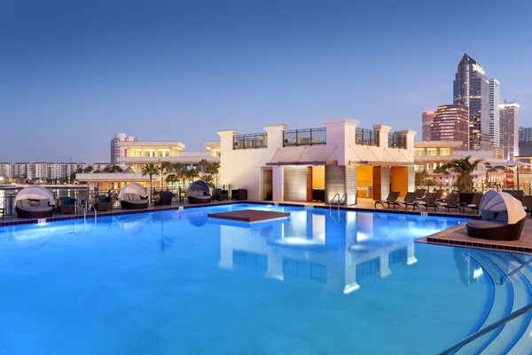 Luxury waterfront view of Tampa Marriott Water Street featuring modern high-rise architecture, stylish outdoor pool area, palm trees, and vibrant downtown Tampa skyline near the marina.