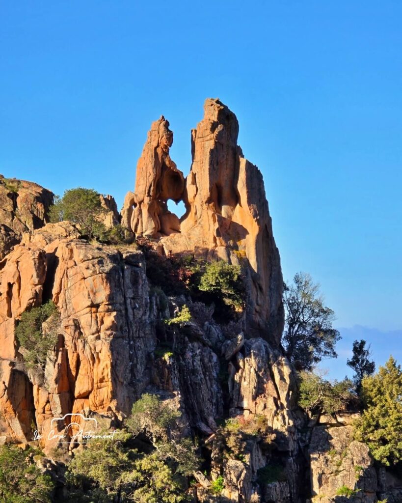 Red granite cliffs and green hillsides in the Calanques de Piana during spring