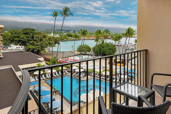 Waterfront view of Courtyard King Kamehameha's Kona Beach Hotel in Kailua-Kona, Hawaii, featuring direct beach access, modern guest rooms, tropical palm trees, and picturesque views of Kailua Bay.