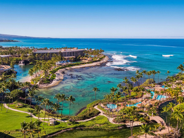 Family-friendly view of Hilton Waikoloa Village on Hawaii's Big Island, featuring tropical pools, waterslides, lagoons, palm trees, and spacious resort grounds ideal for family vacations.