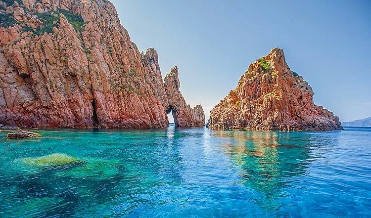 Traveler photographing the red cliffs of Scandola Nature Reserve from a boat