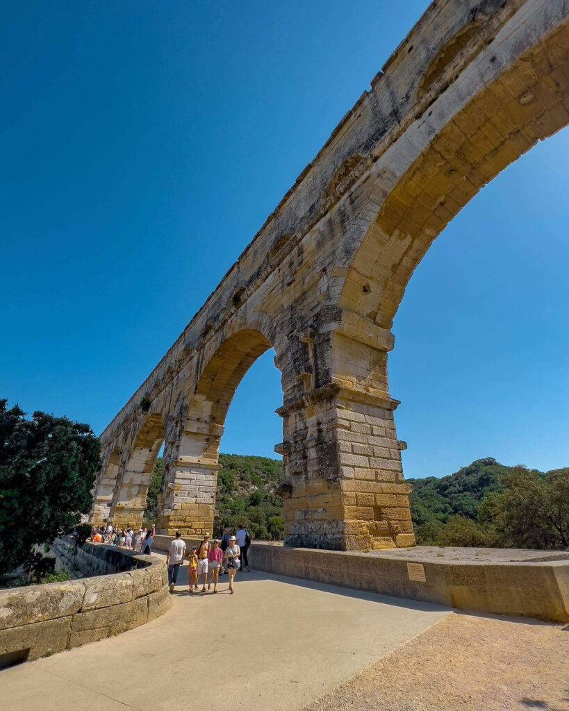 Visitors walking beside the arches of Pont du Gard Roman aqueduct