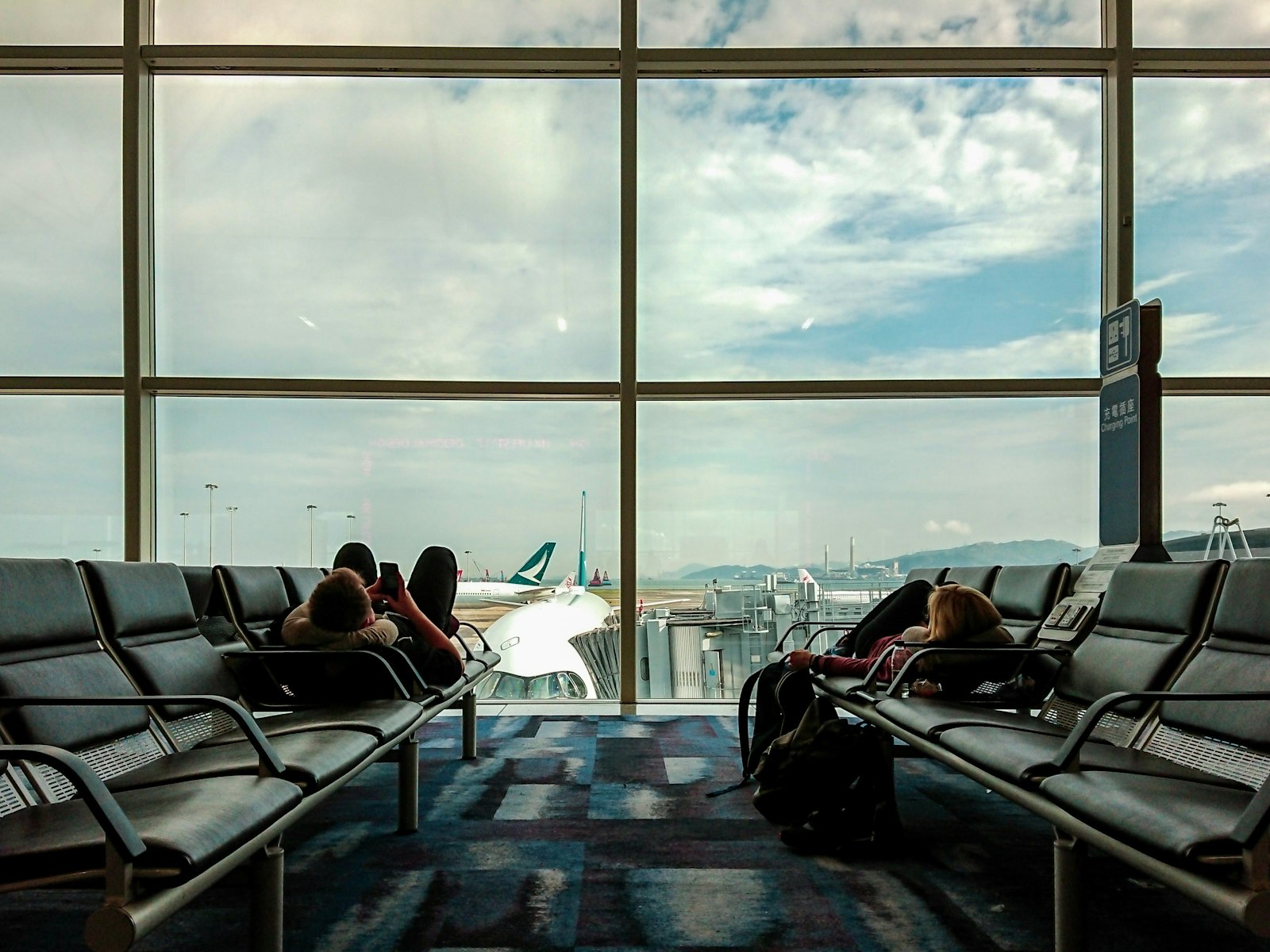 Travelers pulling luggage through a sunlit airport terminal during flight delays