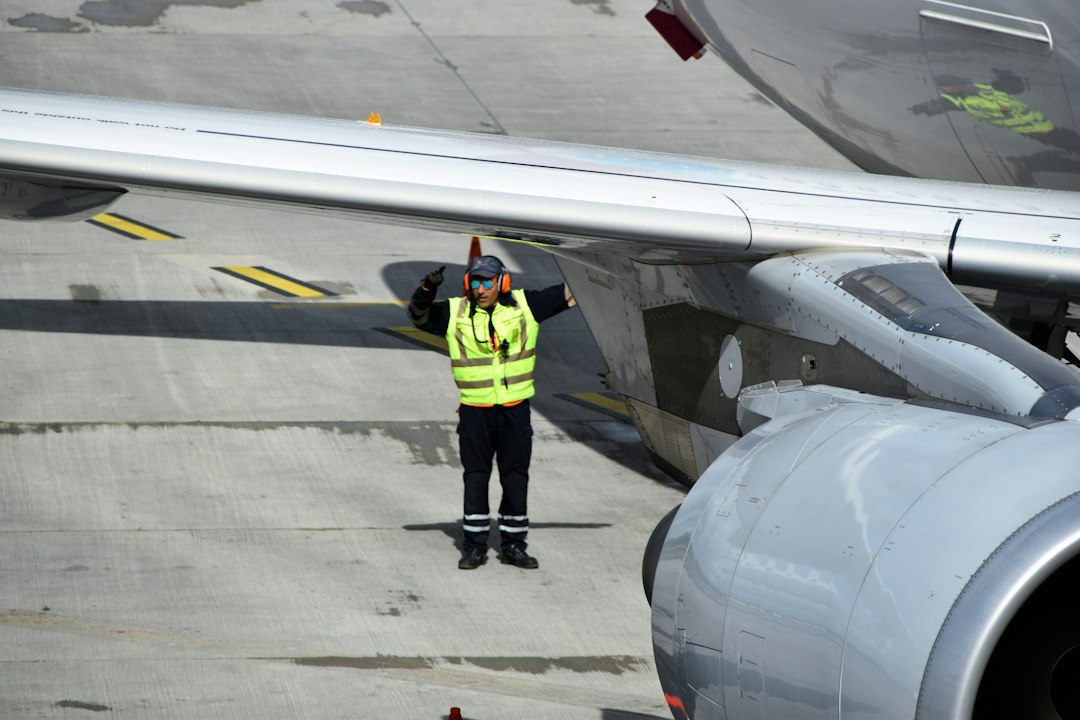 Ground crew worker in a high-visibility vest directing an aircraft on the tarmac beside the wing and engine