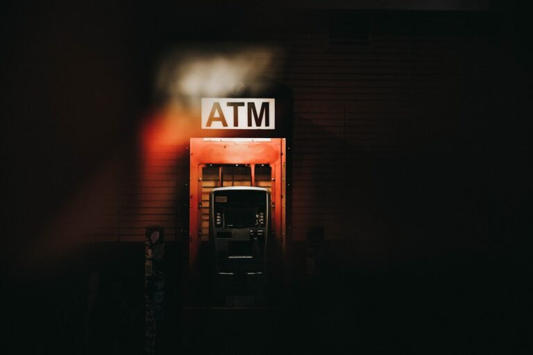 An illuminated ATM cash machine on a city street at night.