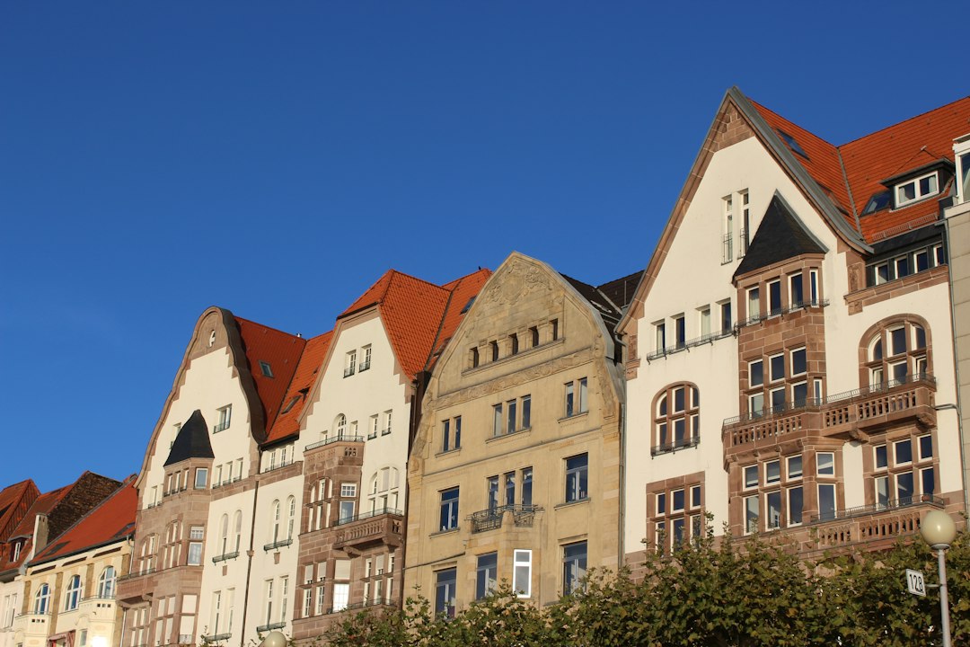 A quiet German residential street lined with pastel apartment buildings under a blue sky