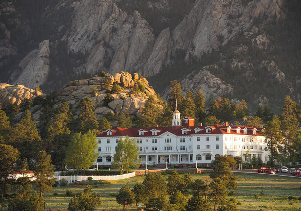 Historic exterior view of The Stanley Hotel in Estes Park, Colorado, featuring its iconic white facade, red roof, grand architecture, and scenic Rocky Mountain backdrop.